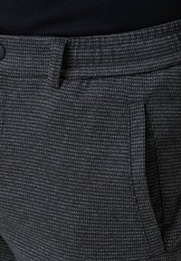 Dark grey textured trousers with a buttoned waistband, belt loop, and side pocket, worn with a black top.