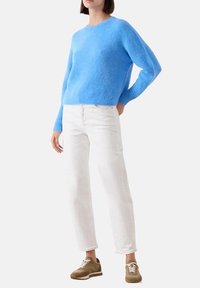 Maglione blu soffice con maniche lunghe, scollo rotondo, abbinato a jeans bianchi e sneaker marroni, creando un outfit casual e complementare.