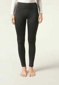 Svarta tights i elastiskt material, med hög midja och en slät yta, som sitter tajt genom benen ner till ankeln.