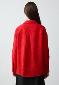 Rotes Leinenhemd mit lockerer Passform, geknöpften Manschetten und einer Rückenausschnitt, mit einem leicht abgerundeten Saum und einem Kragen.