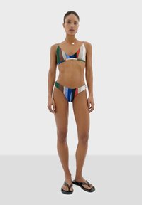 Bikini set v mnohých farbách s pruhovaným vzorom. Materiál má hladkú textúru; trojuholníkový top a nohavičky s nízkym pásom. Spárované s čiernymi žabkami.
