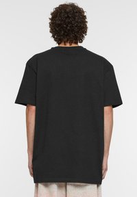 Juoda medvilninė marškinė su laisvu kirpimu ir trumpomis rankovėmis, turinti apvalų iškirpimą ir šoninius įpjovimus prie są mowing, kad būtų lengviau judėti.