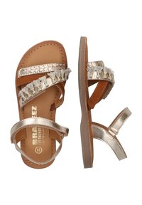 Bruine leren sandalen met een metalen gouden band, voorzien van gevlochten accenten en stoffen franjes. Platte zool, verstelbare enkelband.