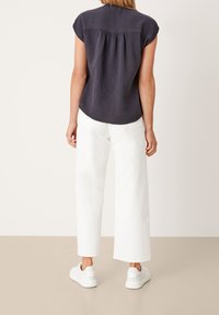 Haut bleu marine à manches courtes en tissu texturé avec froncements à l'arrière, associé à un pantalon large blanc et des baskets blanches.