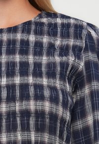 Primo piano di una camicia di stoffa a plaid blu navy e bianco con cuciture arricciate sulle spalle e sulla parte superiore della schiena.