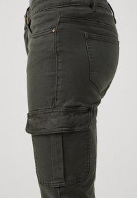 Pantalones cargo en verde oscuro, hechos de tela suave, con bolsillos laterales y un diseño ajustado con costuras detalladas.