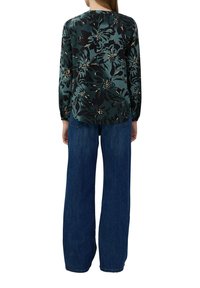 Rückansicht einer langärmeligen Bluse mit Blumenmuster in Dunkelgrün und Schwarz, kombiniert mit hellblauen, weit geschnittenen Jeans. Die Bluse hat gesmokte Ärmel und einen gesmokten Kragen.