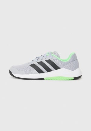 Chaussure de sport gris clair avec des bandes noires, une doublure intérieure verte et des accents blancs et verts sur la semelle, vue de profil sur un fond uni.