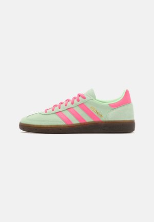 Baskets Adidas à profil bas en suède vert clair avec des bandes roses, des lacets, un languette de talon et une semelle en gomme, vue de côté sur fond blanc.