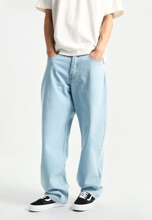 Jeans de mezclilla azul claro con un corte relajado, que cuentan con bolsillos frontales y un diseño de pierna recta. Combinados con zapatillas negras y blancas.