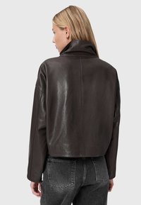 Brūns ādas īss mētelis ar spīdīgu apdari, plašu apkakli un nokristām plecu šuvēm, apvienots ar augsto jostasvietu pelēkajām džinsiem.