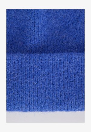 Bonnet tricoté bleu avec une texture douce et duveteuse. Présente des détails côtelés et un bord inférieur roulé, fabriquée en laine épaisse.