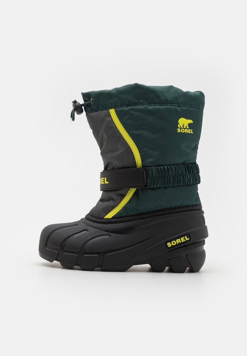 Botte d'hiver pour enfant en noir et vert foncé avec des accents jaunes, une sangle ajustable et une fermeture à cordon, arborant les logos Sorel.