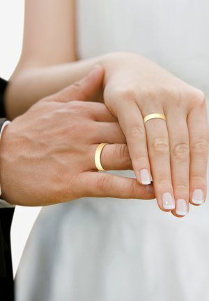 Gold wedding bands are worn on a hand with light skin and manicured nails, showcasing a smooth, polished finish. The background is neutral.