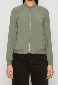 Ljusgrön bomberjacka med dragkedja fram, ribbade ärmslut och nederkant, samt sidofickor. Tillverkad av slät tyg med en minimalistisk design.