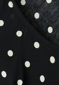 Tissu noir à pois blancs espacés uniformément, avec une couture et une légère variation de texture entre deux sections de tissu.