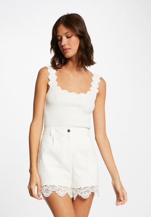 Débardeur blanc à côtes avec encolure festonnée, associé à un short blanc avec une finition en dentelle au bas. Texture lisse et coupe ajustée.