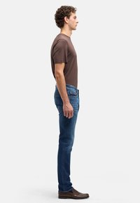 Brązowy bawełniany T-shirt w połączeniu z niebieskimi jeansami denim. Jeansy mają dopasowany krój i subtelne detale przeszyć. Dopełnieniem stroju są brązowe skórzane buty.