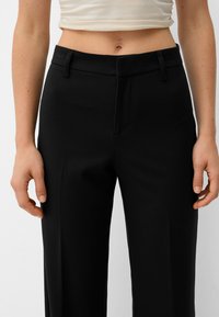 Black tailored pants with a smooth, matte texture, featuring a flat front, belt loops, and side pockets. The fabric appears lightweight and structured.