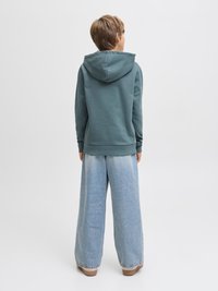 Hanorac turcoaz cu glugă mare, asortat cu pantaloni largi din denim bleu deschis. Textură netedă, design casual. Văzut din spate.