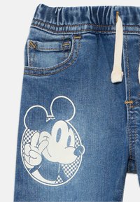 Pantalon en denim avec une taille élastique et un cordon de serrage blanc, arborant un motif graphique blanc de Mickey Mouse faisant un signe de paix.