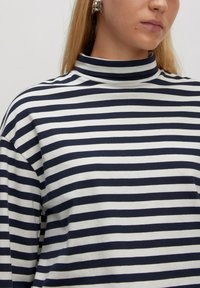 Gestreiftes T-Shirt mit Rollkragen in Marineblau und Weiß, aus weichem Stoff gefertigt; verfügt über einen Kunstkragen und eine lockere Passform, mit weiten Ärmeln und einer flachen Textur.