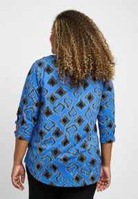 Zila blūze ar rakstu un 3/4 piedurknēm, ar ģeometrisku dizainu melnā un gaišākā zilā krāsā, gluda auduma ar nelielu spīdumu.