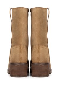 Las botas tobilleras de ante marrón presentan una puntera redondeada, costuras laterales, una textura sutil y un tacón de madera apilada. Incluyen lengüetas en la parte trasera.