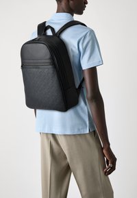 Black backpack with a textured gray lower section, featuring a rounded top, smooth finish, dual shoulder straps, and a front zip pocket.