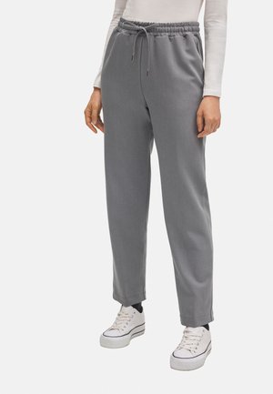 Pantalones de chándal grises, ajustados en la parte inferior, con una cinturilla elástica y cordón. Textura suave, con bolsillos laterales, combinados con zapatillas blancas.