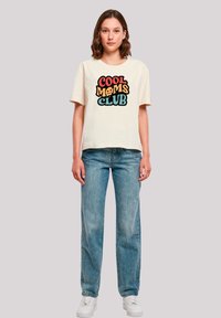 Cream short-sleeve t-shirt with "COOL MOMS CLUB" in multi-colored text. Worn with light blue straight-leg jeans and white sneakers.