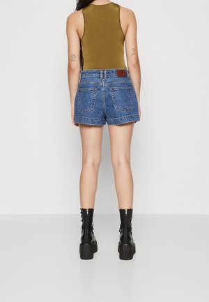 Jeansshorts med hög midja, blå färg och fransig fåll, kombinerade med en olivgrön linne och svarta snörstövlar i ankellängd.