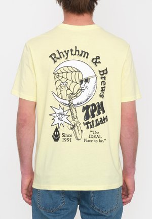 Camiseta de algodón amarilla con gráfico impreso que presenta una luna tocando el saxofón, el texto "Rhythm & Brews" y detalles en negro.