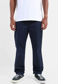 Pantalon décontracté bleu marine à coupe droite, fabriqué en tissu résistant ; associé à des baskets noires. T-shirt blanc uni porté par-dessus.