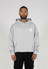 Sudadera gris con capucha y bolsillo frontal, de corte holgado, y detalle gráfico en blanco en el pecho. Tejido texturizado con un acabado suave.