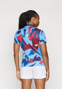 Koszulka polo z krótkim rękawem w kolorze niebieskim z wielobarwnym wzorem geometrycznym, zawierającym akcenty w kolorze czerwonym, granatowym i żółtym. Gładki, lekki materiał.