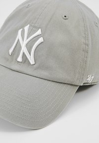 Grey baseball cap made of cotton twill. Features a white embroidered NY logo, curved brim, and a stitched texture. 47 brand tag on side.