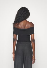 Top nero a spalle scoperte con textura a coste, silhouette aderente, abbinato a pantaloni grigi a vita alta con due bottoni posteriori.