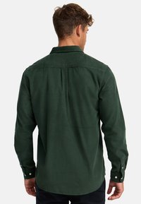 Grüne Cordhemd mit einem Button-Down-Kragen, langen Ärmeln, gefaltetem Rücken und subtiler Textur. Verfügt über kontrastierende Knöpfe an den Manschetten.
