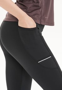 Zwarte sportleggings van rekbaar materiaal, met een zijzak en een witte accentstrook, en flatlock naden voor comfort.