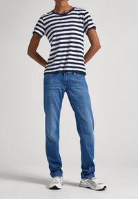 Marinblå och vit randig bomullströja, avslappnad passform. Kombinerad med ljusblå denimjeans och grå sneakers. Avslappnad, vardaglig klädsel.