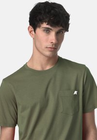 T-shirt verde oliva in tessuto di cotone, con scollatura rotonda, maniche corte e taschino sul lato sinistro con un accento di logo bianco.