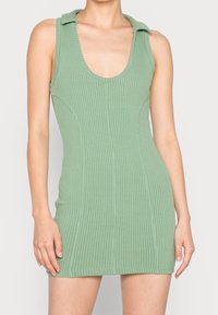 Žebrované zelené šaty s kulatým výstřihem a límcem, přiléhavého střihu, vyrobené z texturované látky, sahající do poloviny stehna.