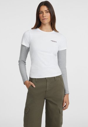 White short-sleeve t-shirt with gray long sleeves underneath; features a small black logo on the chest. Paired with olive green cargo pants.