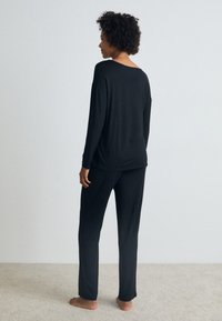 Svart loungewear-set bestående av en lössittande långärmad topp och matchande byxor, tillverkat av mjukt tyg, visat mot en neutral bakgrund.