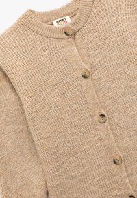 Beige neulottu kardigan, jossa on pyöreä kaula-aukko, neljä suurta nappia ja ribbauskintaat. Valmistettu pehmeästä, teksturoidusta puuvillamateriaalista.