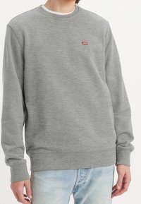 Sudadera gris hecha de una tela suave, con un cuello redondo y mangas largas. Contiene un pequeño logo rojo de Levi's en el lado izquierdo del pecho.