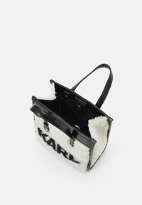 Sac à main en cuir noir avec des accents en fourrure blanche douce, arborant le mot "KARL" en noir, au design ouvert, et deux anses.
