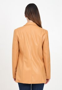 Blazer in finta pelle beige con un design strutturato, rever affilati e dettagli a cucitura verticale. La vista posteriore mostra una texture liscia e linee pulite.