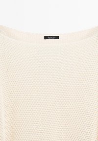 Jasno beżowy sweter dzianinowy z luźnym, szerokim dekoltem i fakturowanym wzorem. Ozdobiony czarną metką z napisem "Massimo Dutti" przy kołnierzu.